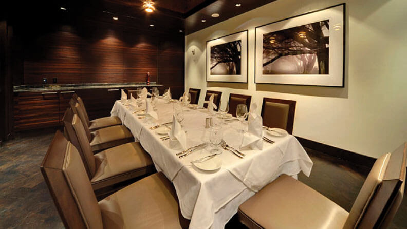 A long table set surrounded by tan and brown chairs and set with white linens inside Final Cut Steakhouse at Hollywood Casino in St. Louis, Missouri.