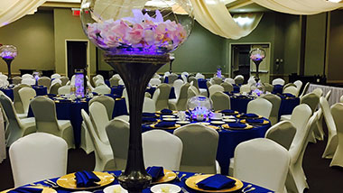 A wedding reception featuring table rounds and tall fish bowl centerpieces in white and dark blue.