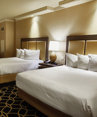Two queen-size beds and a desk with chair inside the Rodeo 2 Queens hotel room at Hollywood Casino in St. Louis, Missouri.