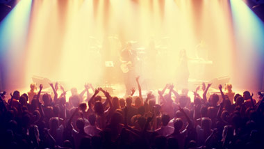 band on concert stage with concert goers listening with hands in the air