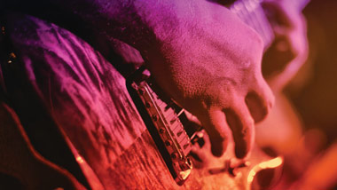 close up of hand playing guitar with pink, purple and gold overtones